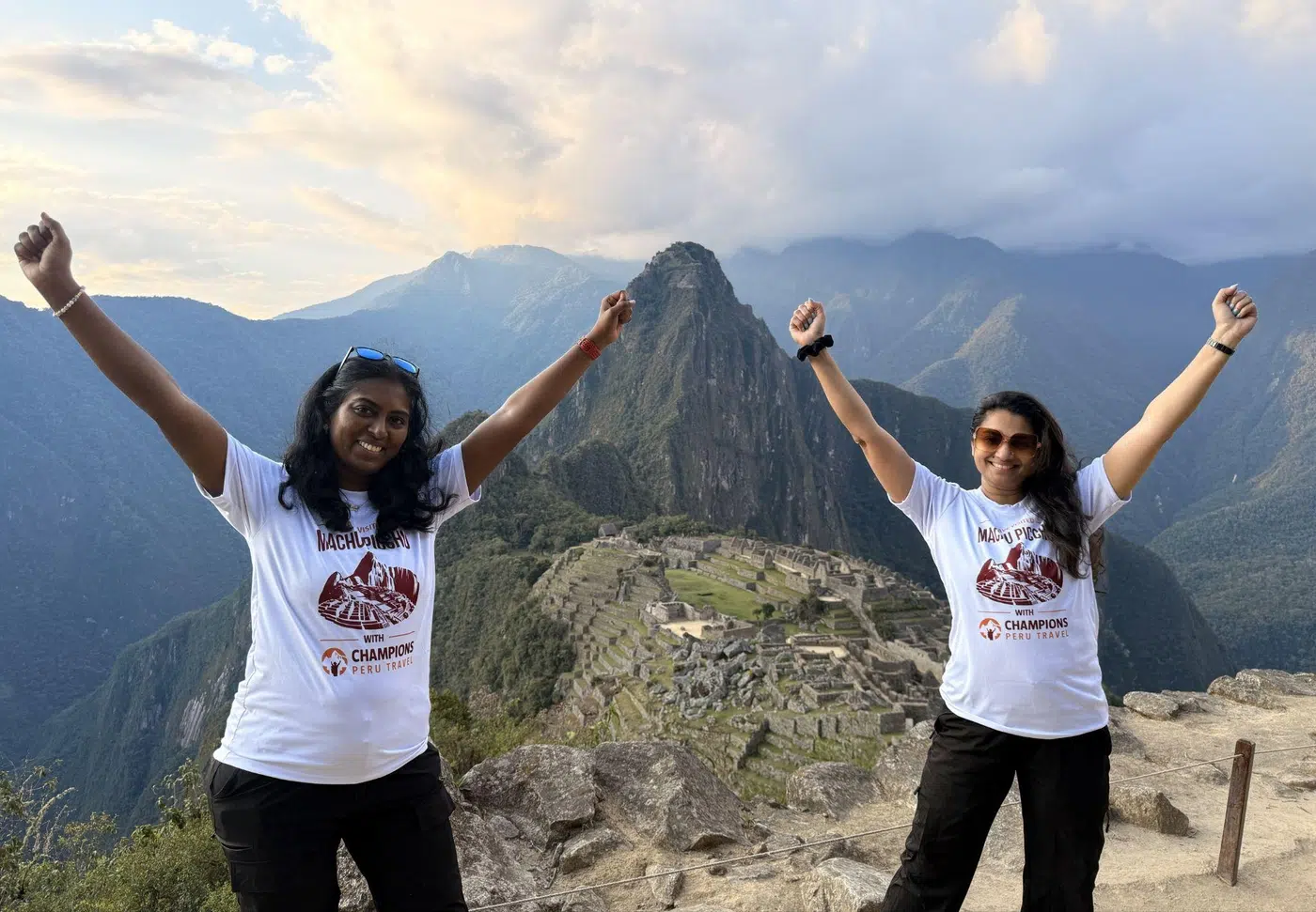 Two travelers celebrating at the Machu Picchu viewpoint with the ancient Inca citadel in the background